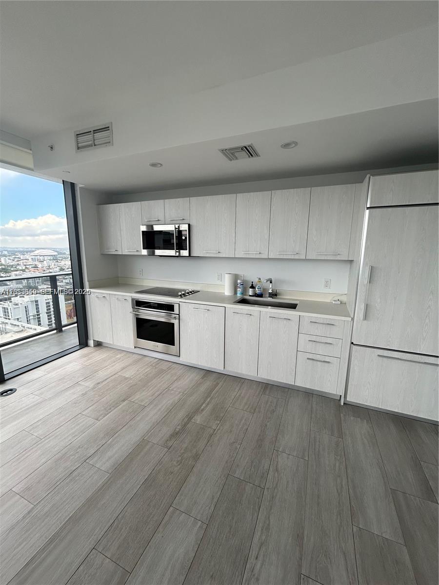 A modern kitchen features light wood-grain cabinets, stainless steel appliances, and floor-to-ceiling windows — 55 SW 9th St # 3506, Miami FL 33130, MIAMI, FL