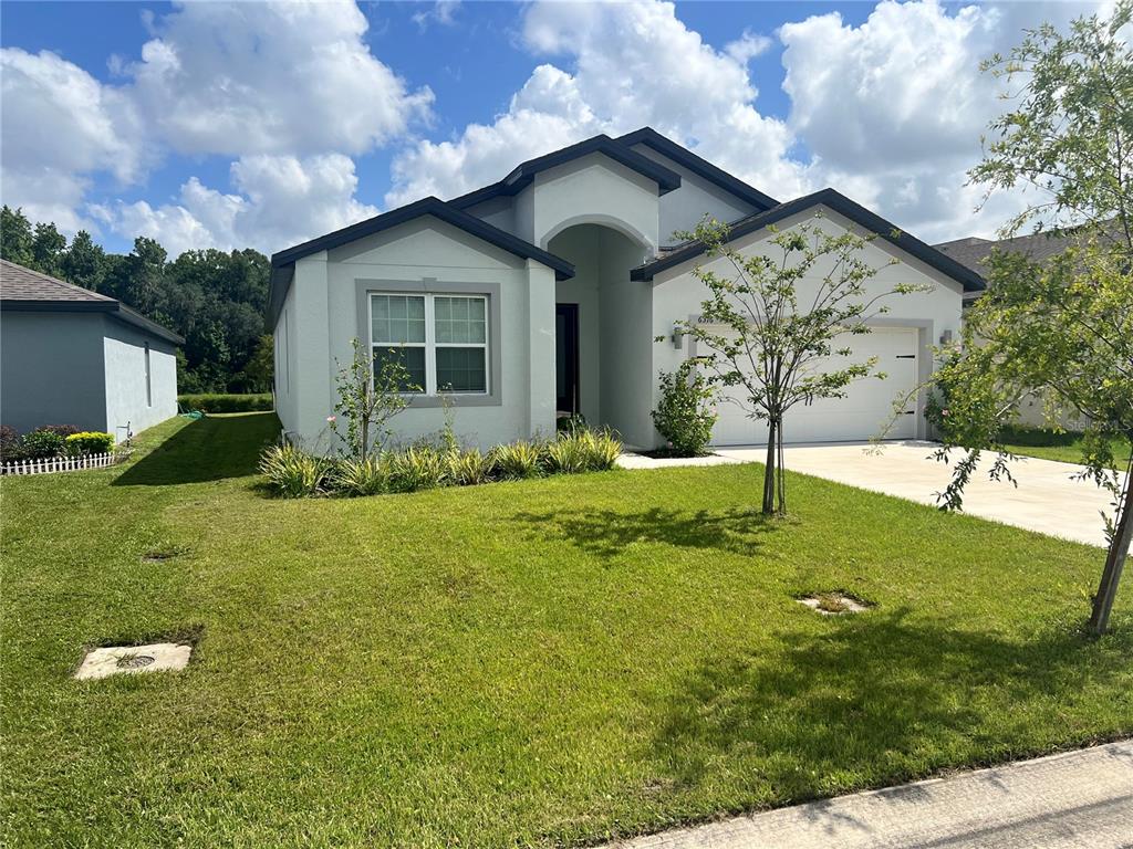 A single-story house with a light-colored stucco exterior, a two-car garage, and a front lawn — 6316 DOLOSTONE DRIVE, LAKELAND, FL