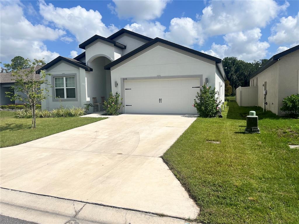 A single-story house with a white stucco exterior, a two-car garage, and a concrete driveway — 6316 DOLOSTONE DRIVE, LAKELAND, FL