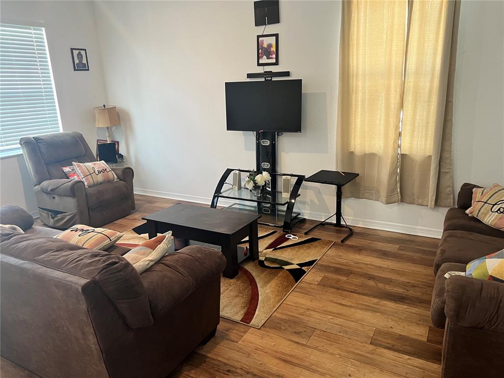 A living room features brown furniture, a television stand, and wood-look flooring — 6316 DOLOSTONE DRIVE, LAKELAND, FL