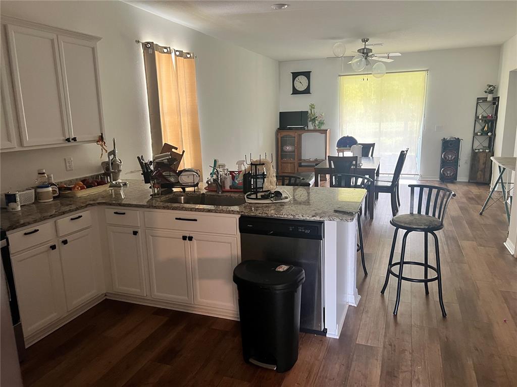 A kitchen with white cabinets and granite countertops overlooks a dining area with wood flooring — 6316 DOLOSTONE DRIVE, LAKELAND, FL