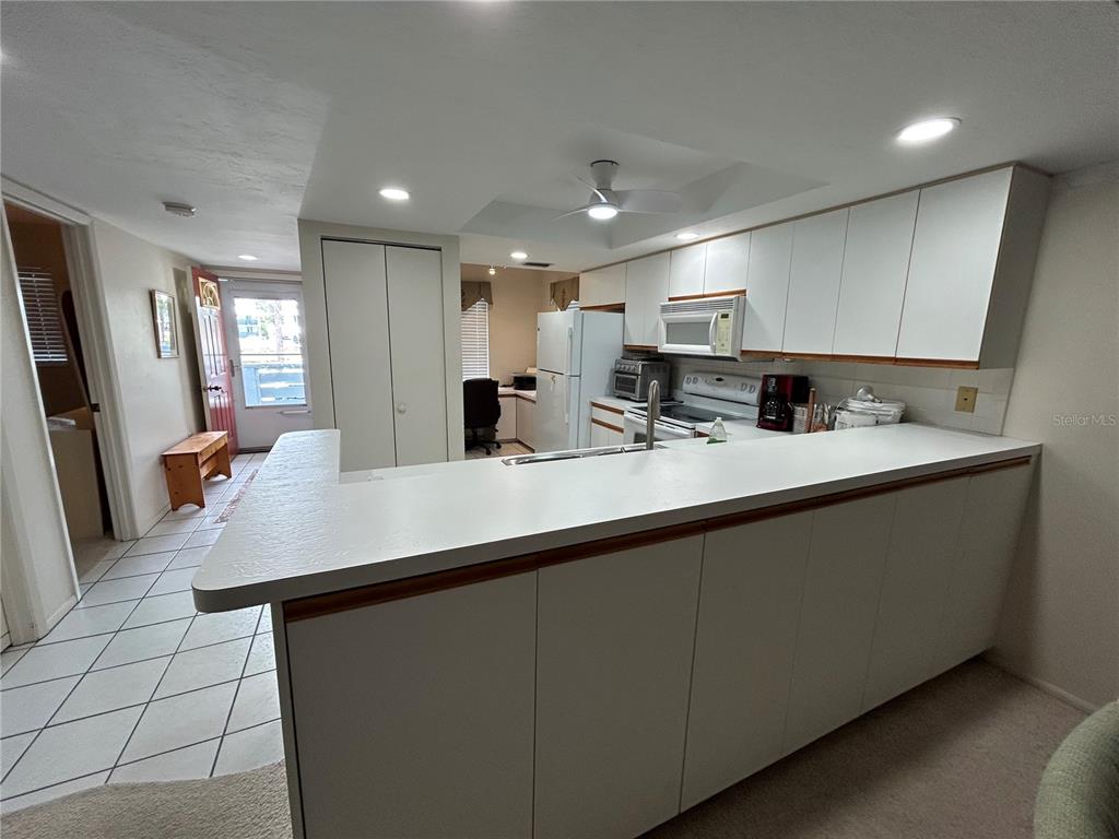 A kitchen features white cabinetry, a breakfast bar, and a tiled floor leading to a doorway — 6800 PLACIDA ROAD UNIT 162, ENGLEWOOD, FL