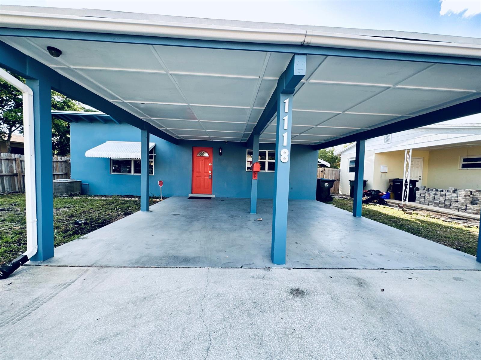 A blue house features a large concrete carport and a bright orange front door — 1118 N E Street, FL 33460, FL