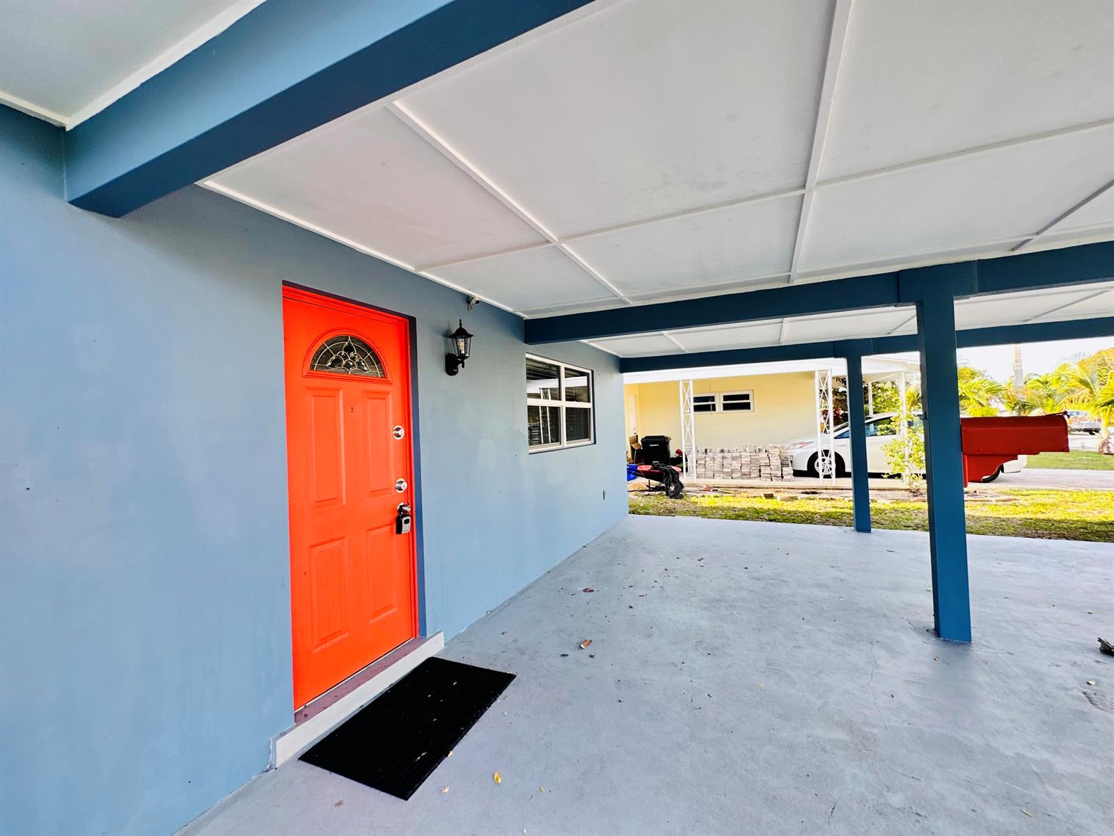 A blue exterior wall features a bright orange front door under a covered carport — 1118 N E Street, FL 33460, FL