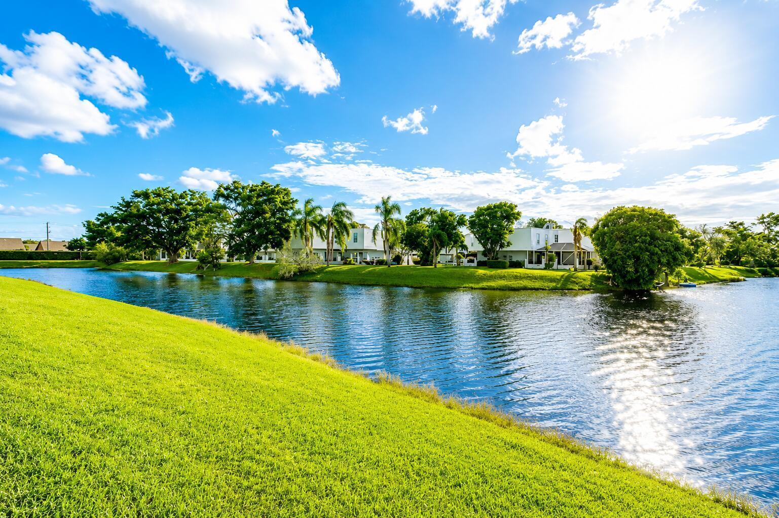 A grassy lawn slopes down to a pond in front of white residential buildings — 1512 Shaker Circle, Wellington FL 33414, WELLINGTON, FL