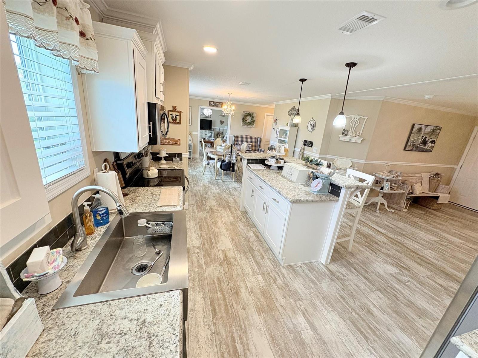 A kitchen features white cabinets, granite countertops, a stainless steel sink, and wood-look flooring — 4331 SW 10th Way, Okeechobee FL 34974, OKEECHOBEE, FL