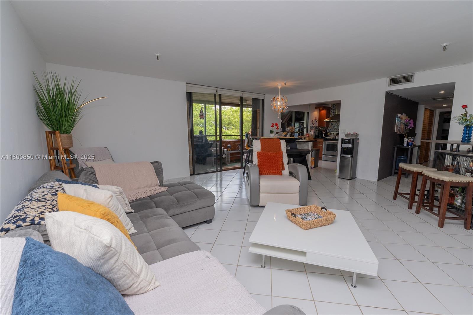 A living room features a gray sectional sofa, white tile flooring, and a sliding glass door — 665 NE 195th St # 419, Miami FL 33179, MIAMI, FL