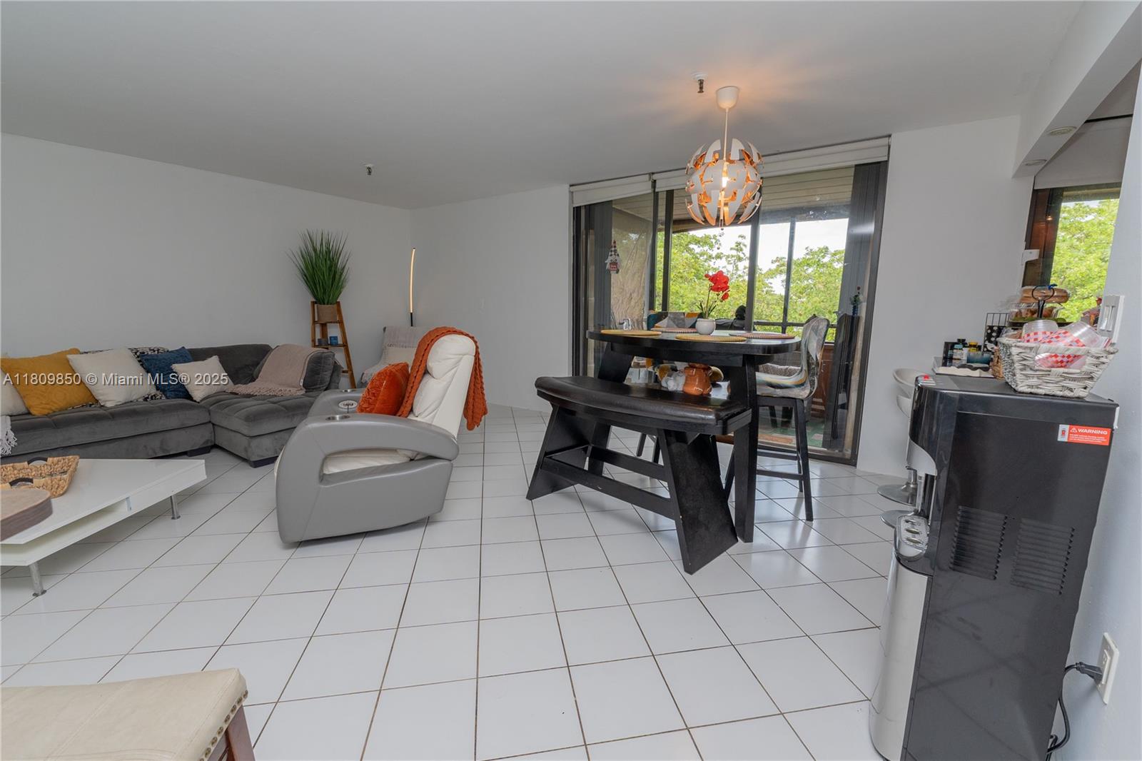 A living and dining area features white tile floors, a sectional sofa, and a dining set — 665 NE 195th St # 419, Miami FL 33179, MIAMI, FL
