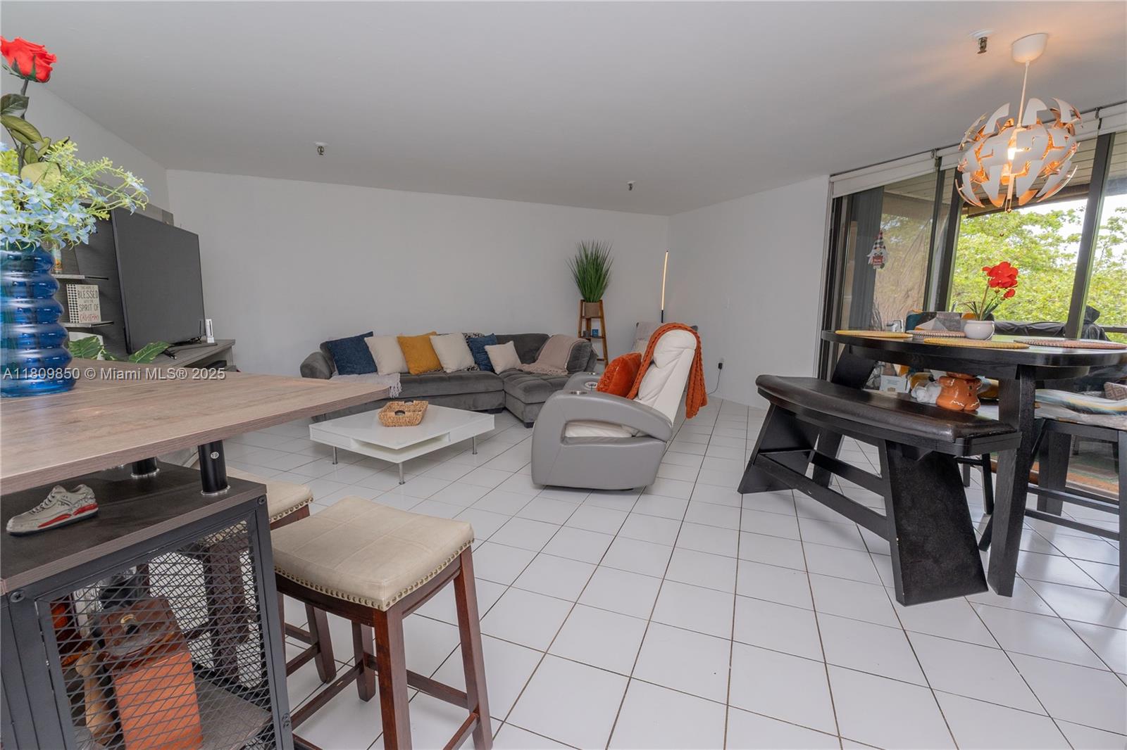An open-concept living and dining area features white tile floors, a sectional sofa, and furniture — 665 NE 195th St # 419, Miami FL 33179, MIAMI, FL