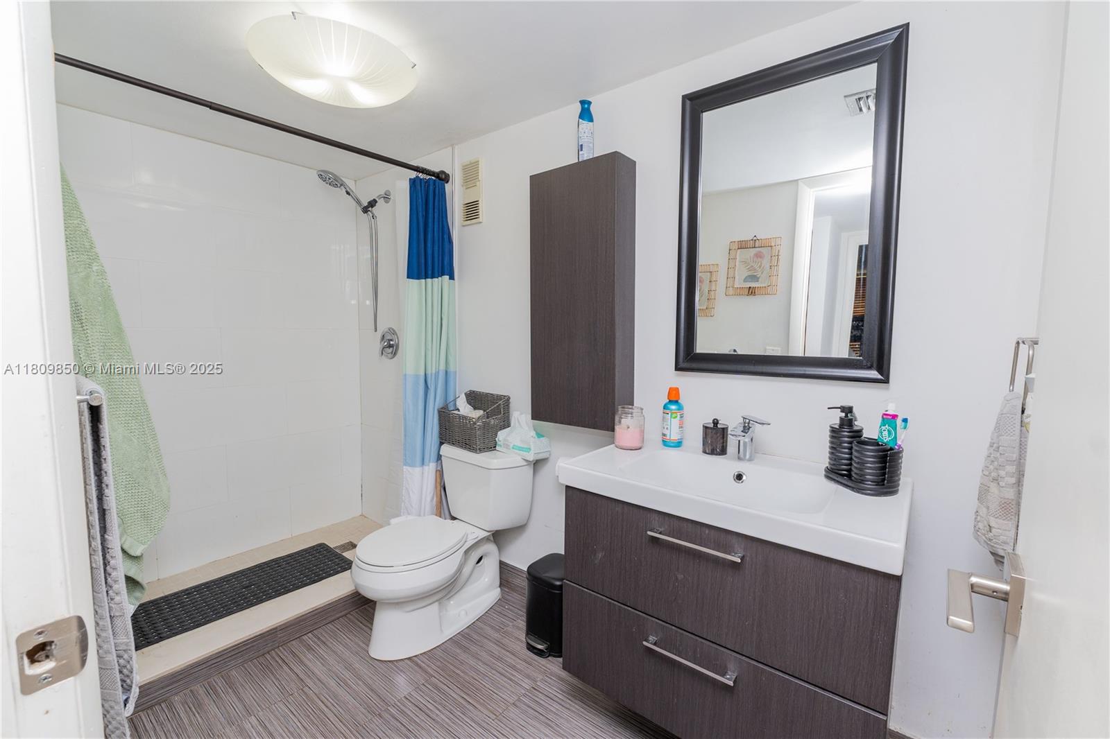 A bathroom features a walk-in shower, a toilet, a dark wood vanity, and a mirror — 665 NE 195th St # 419, Miami FL 33179, MIAMI, FL
