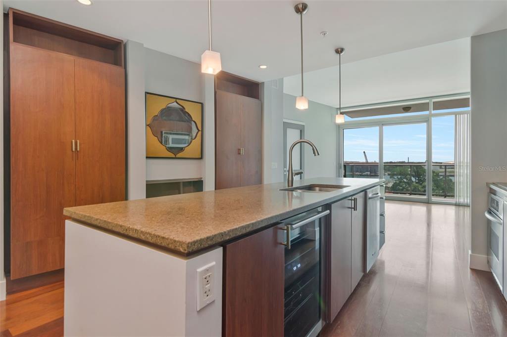 A modern kitchen features a granite-topped island, wood cabinetry, and a view of the outdoors — 111 N 12TH STREET UNIT 1608, TAMPA, FL