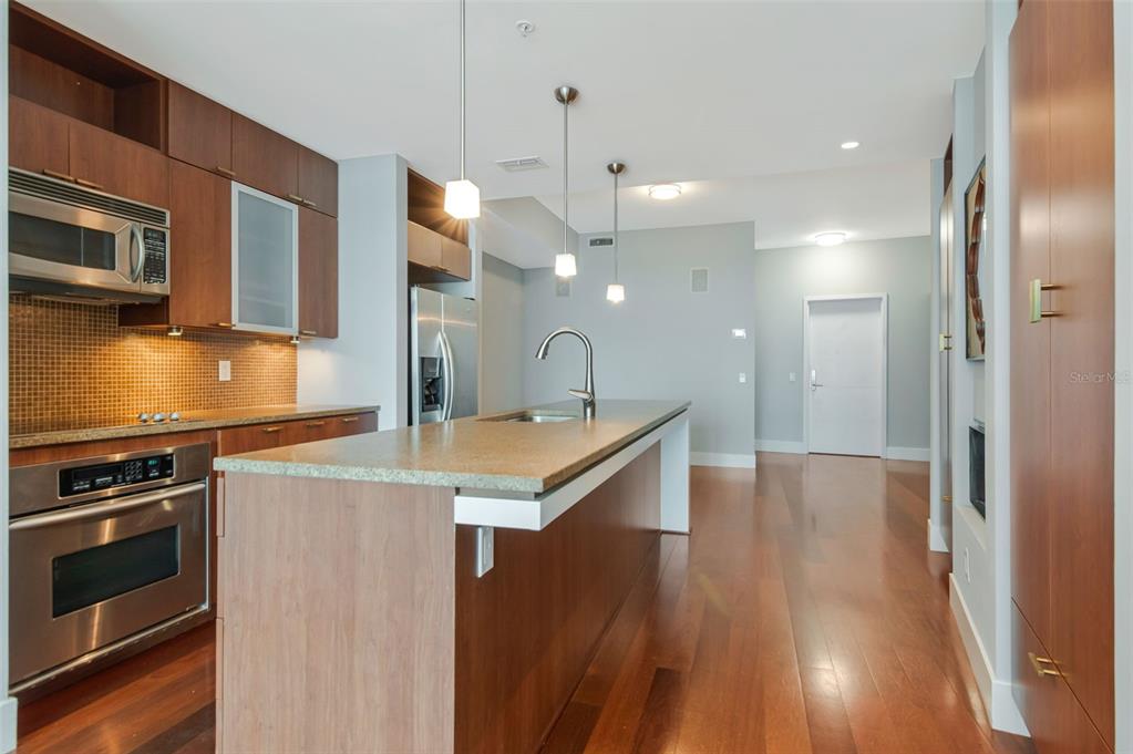 A modern kitchen features wood cabinetry, stainless steel appliances, and a central island with seating — 111 N 12TH STREET UNIT 1608, TAMPA, FL