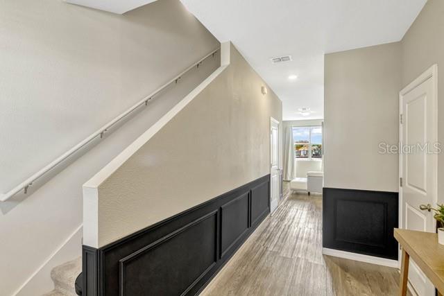 A hallway with light wood flooring, a staircase with a metal railing, and black wainscoting — 125 MANDOVI STREET, DAVENPORT, FL