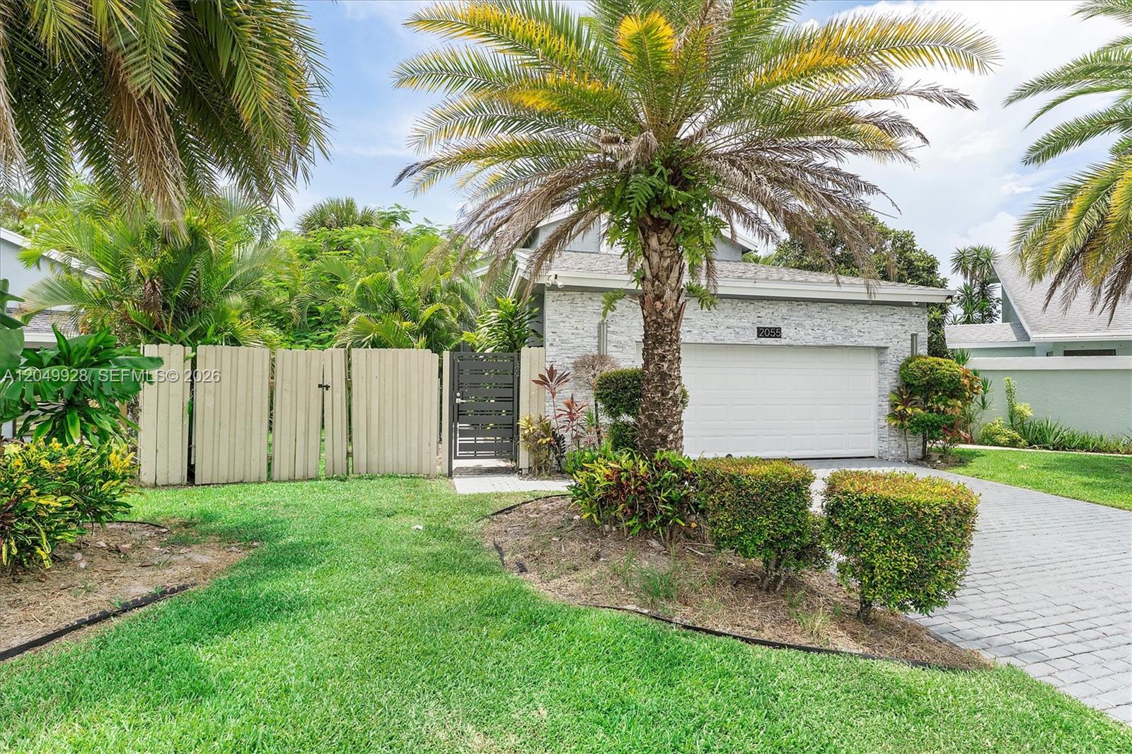 A single-story house features a white stone facade, a two-car garage, and a palm tree — 2055 NW 9th St, Delray Beach FL 33445, DELRAY BEACH, FL