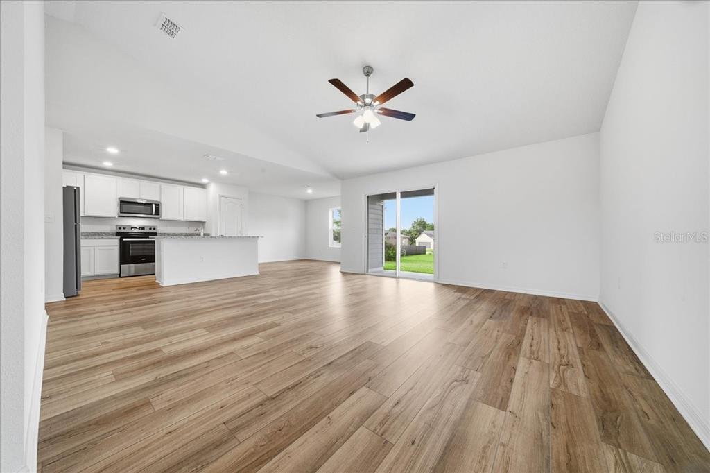 An open-concept living area features light wood-look flooring, a ceiling fan, and an adjacent kitchen — 2722 SW 151 PLACE, OCALA, FL