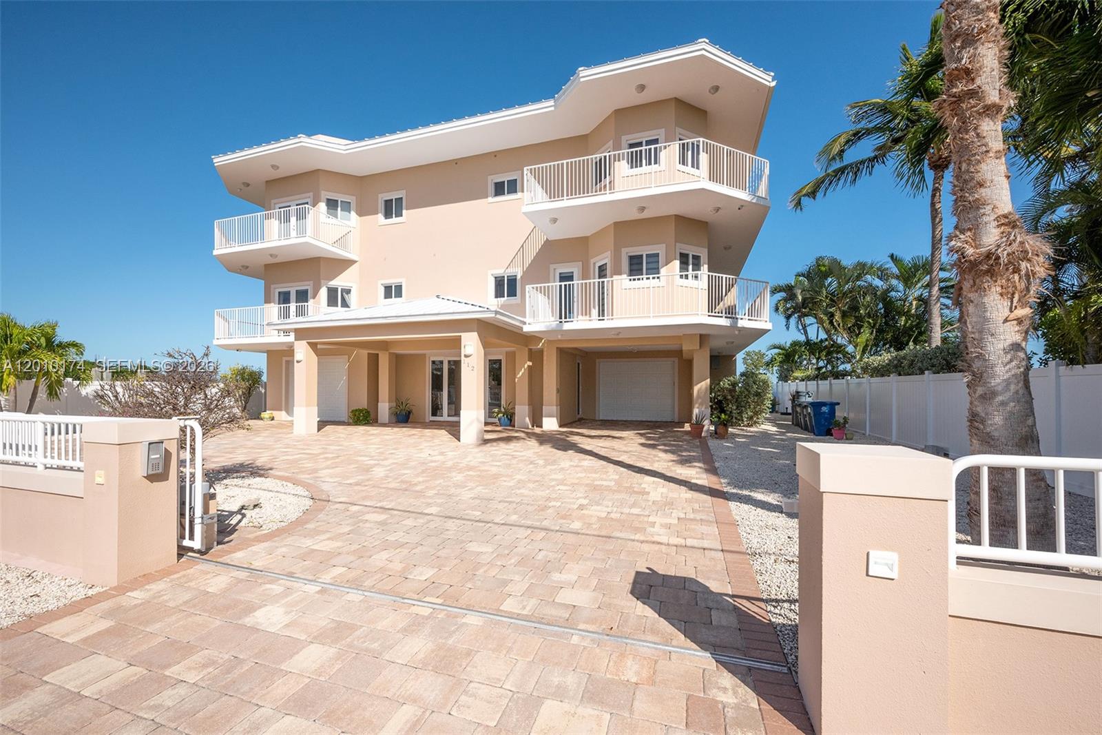 A three-story beige house with multiple balconies stands behind a paved driveway and fence — 112 N Bounty Ln, Key Largo FL 33037, KEY LARGO, FL