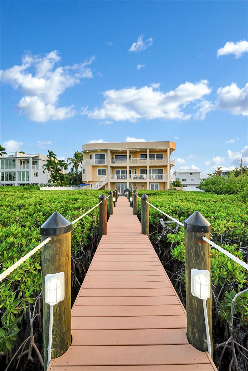A wooden dock leads through a mangrove forest toward a three-story waterfront house — 112 N Bounty Ln, Key Largo FL 33037, KEY LARGO, FL