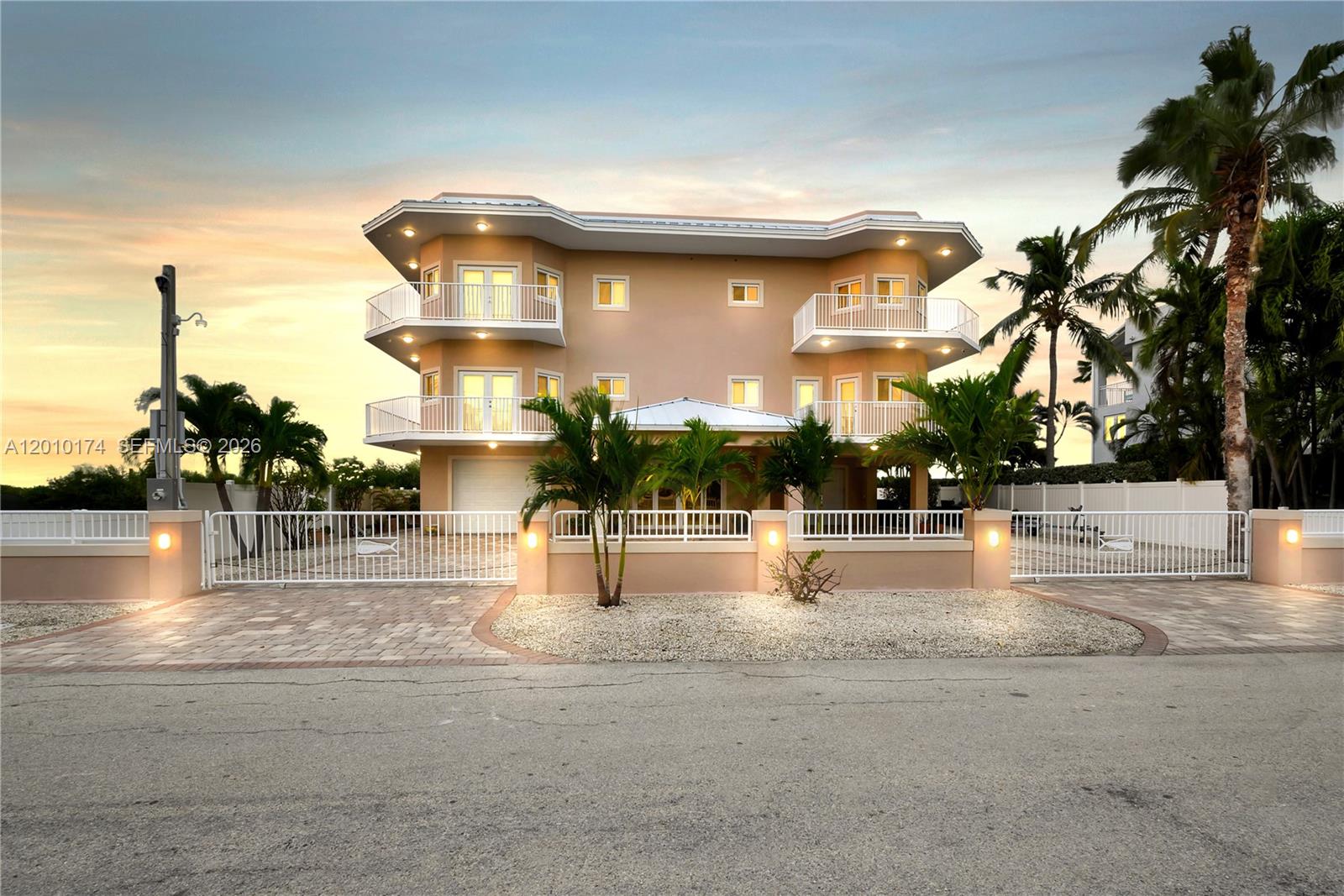 A three-story tan house with white balconies and a gated driveway at sunset — 112 N Bounty Ln, Key Largo FL 33037, KEY LARGO, FL