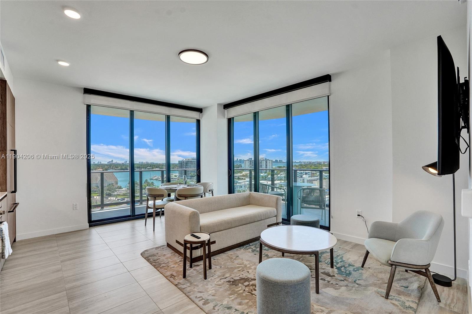 A living room with floor-to-ceiling windows, a beige sofa, and a view of water — 580 72nd St # 810, Miami Beach FL 33141, MIAMI BEACH, FL