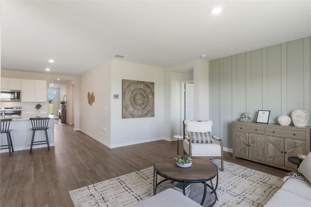 A living room with wood-look flooring, a sage green accent wall, and an open kitchen — 1779 GRANDIOSE DRIVE, HAINES CITY, FL