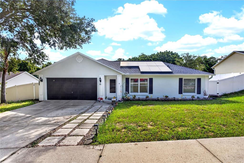 A single-story house with a large tree, a concrete driveway, and a dark garage door — 919 ARBOR HILL CIR, MINNEOLA, FL