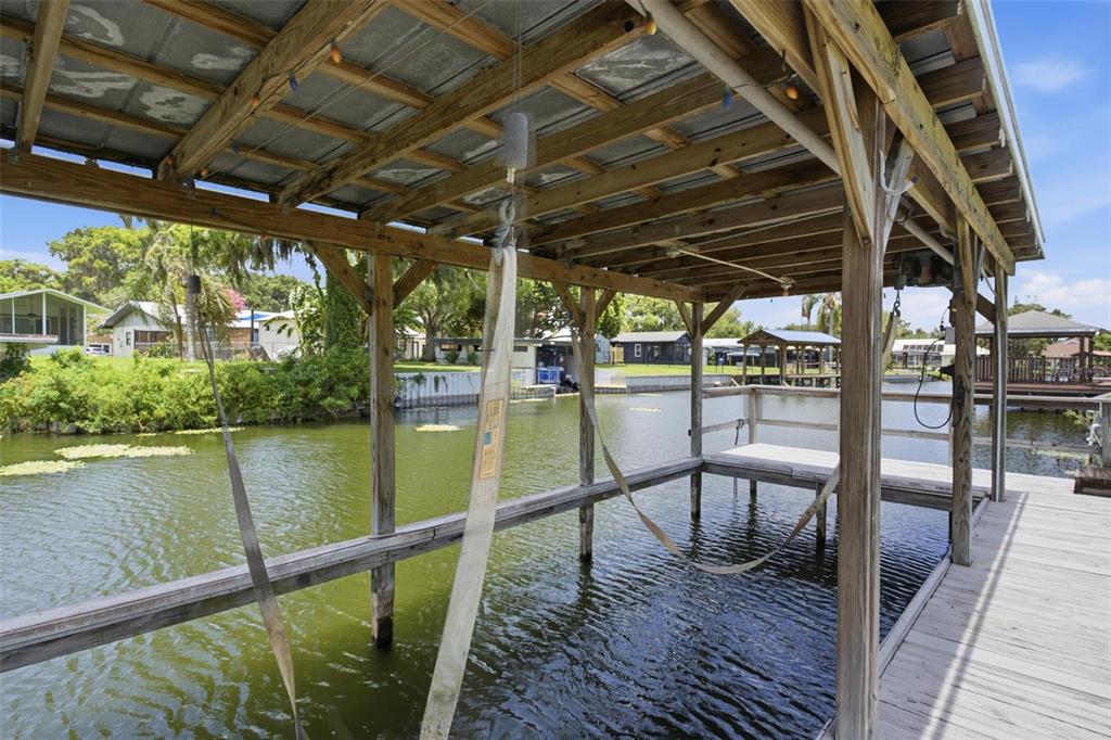 A wooden boat lift structure stands over a canal with a metal roof and slings — 1631 CANAL COURT, TAVARES, FL
