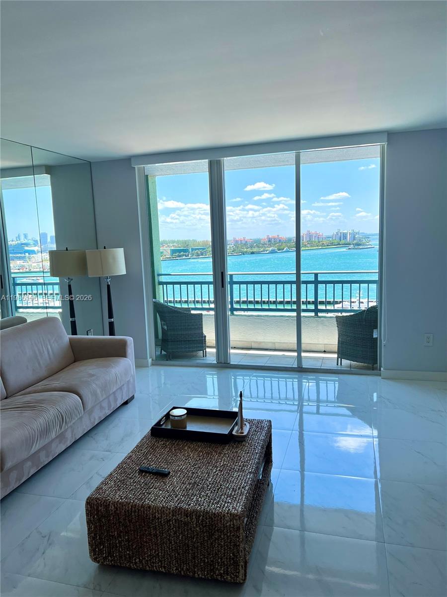 A living room with white tile floors, a sofa, and a balcony overlooking the ocean — 90 Alton Rd # 1106, Miami Beach FL 33139, MIAMI BEACH, FL