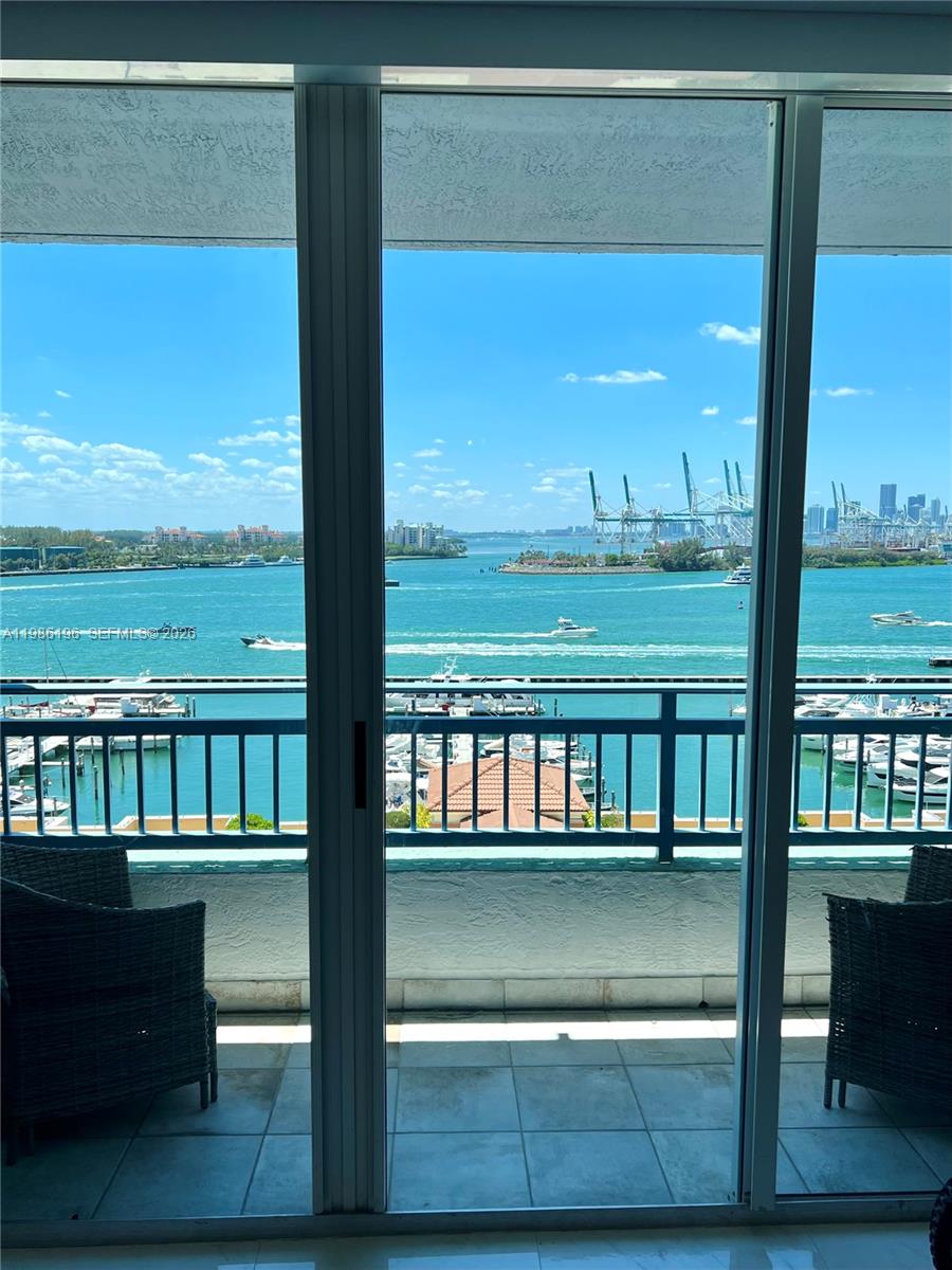 A balcony with wicker chairs overlooks a marina, a bay, and a distant city skyline — 90 Alton Rd # 1106, Miami Beach FL 33139, MIAMI BEACH, FL