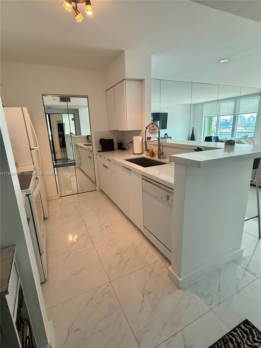 A modern kitchen features white cabinetry, marble-style tile flooring, and a breakfast bar — 90 Alton Rd # 1106, Miami Beach FL 33139, MIAMI BEACH, FL