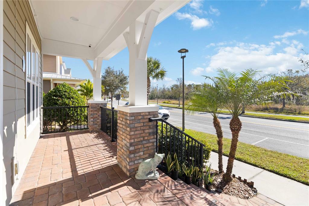 A covered porch with brick flooring, stone-based columns, and a black metal railing — 8905 LAUREATE BOULEVARD, ORLANDO, FL