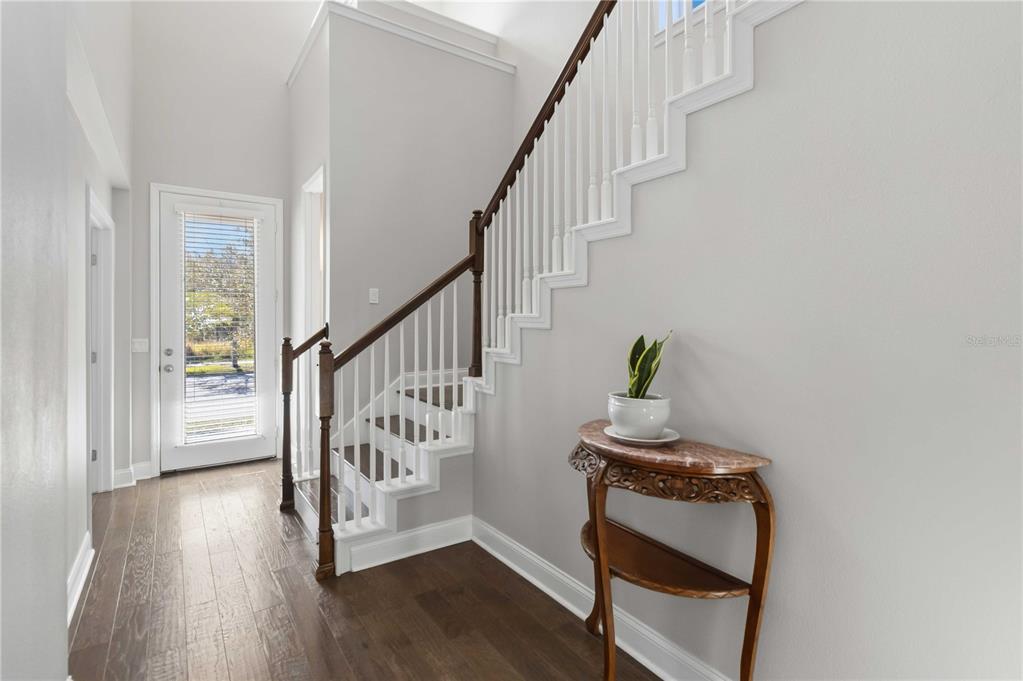 A foyer features hardwood floors, a staircase with white railings, and a marble-topped console table — 8905 LAUREATE BOULEVARD, ORLANDO, FL