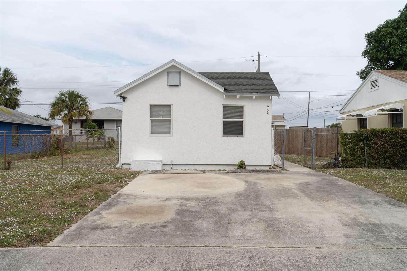 A small, white, single-story house features a concrete driveway and a fenced yard — 908 W 5th Street, Riviera Beach FL 33404, RIVIERA BEACH, FL