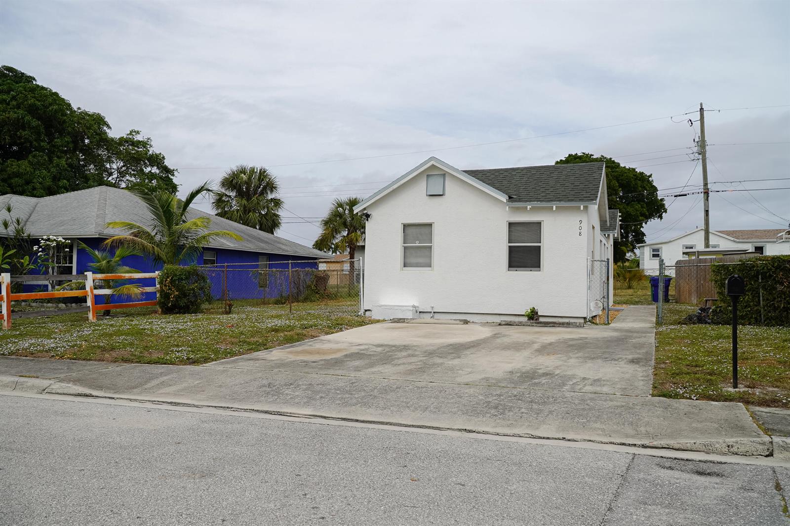 A white single-story house with a concrete driveway sits next to a blue house — 908 W 5th Street, Riviera Beach FL 33404, RIVIERA BEACH, FL