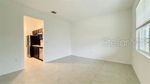 A bright, empty room with light-colored tile flooring leads into a small kitchen area — 905 CITRUS RESERVE BOULEVARD UNIT B, DAVENPORT, FL