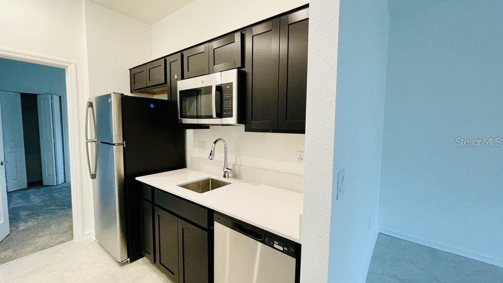 A kitchen features dark cabinets, stainless steel appliances, white countertops, and a sink — 905 CITRUS RESERVE BOULEVARD UNIT B, DAVENPORT, FL