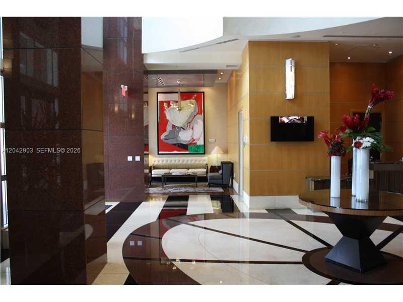 A modern lobby features polished marble floors, wood-paneled walls, a seating area, and a floral arrangement — 244 Biscayne Blvd # 240, Miami FL 33132, MIAMI, FL