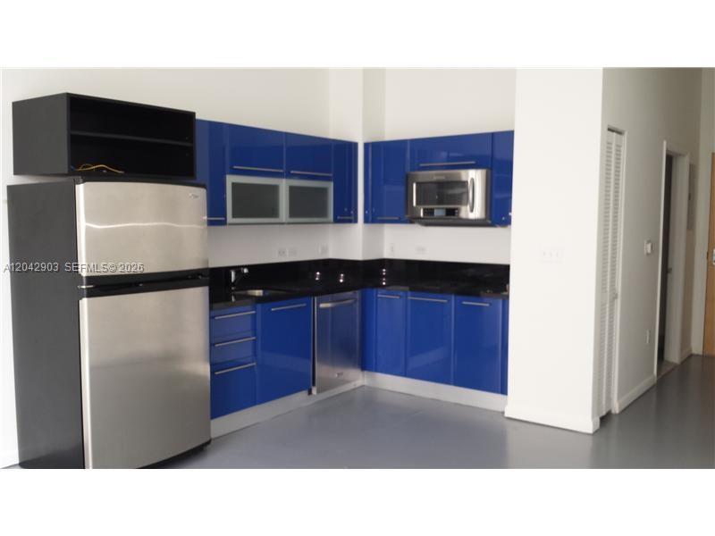 A kitchen features blue cabinets, black countertops, and stainless steel appliances against white walls — 244 Biscayne Blvd # 240, Miami FL 33132, MIAMI, FL