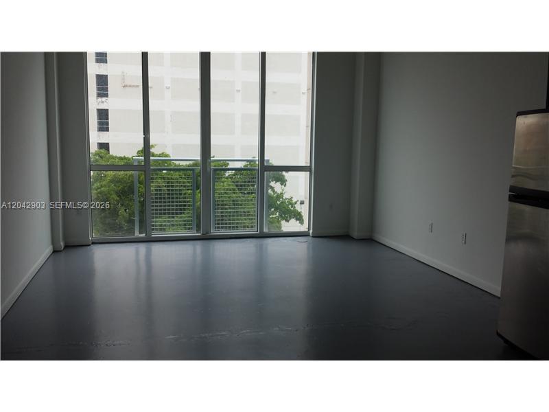 An empty room with gray flooring, white walls, and floor-to-ceiling windows overlooking trees — 244 Biscayne Blvd # 240, Miami FL 33132, MIAMI, FL