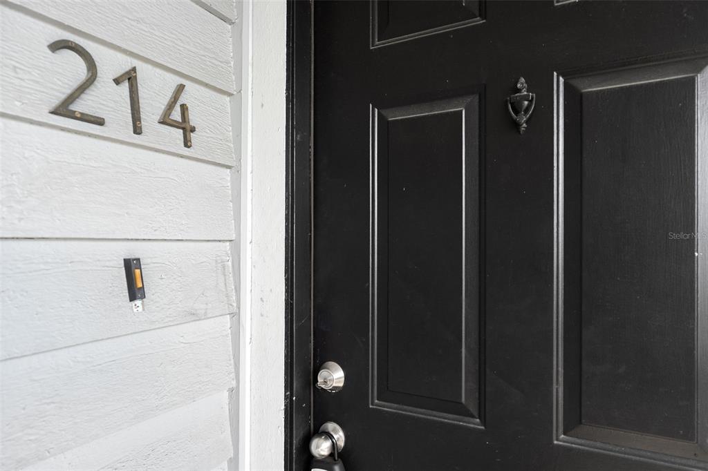 A black front door with a silver knocker is next to white siding displaying number 214 — 3711 W IOWA AVENUE UNIT 214, TAMPA, FL