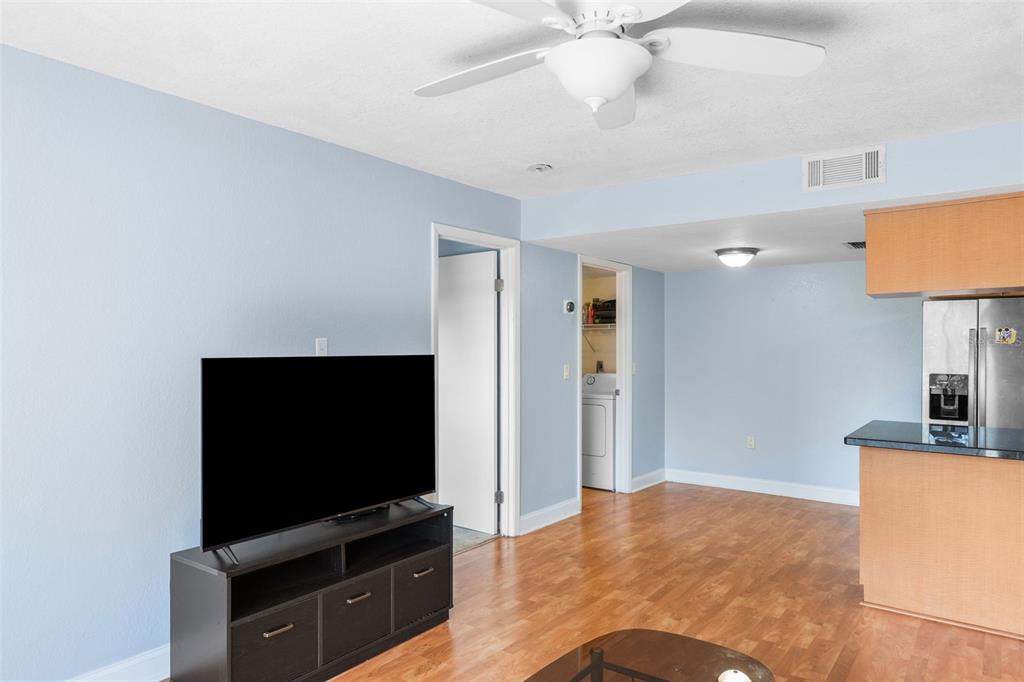 A living room with light blue walls, wood flooring, a ceiling fan, and a television stand — 3711 W IOWA AVENUE UNIT 214, TAMPA, FL