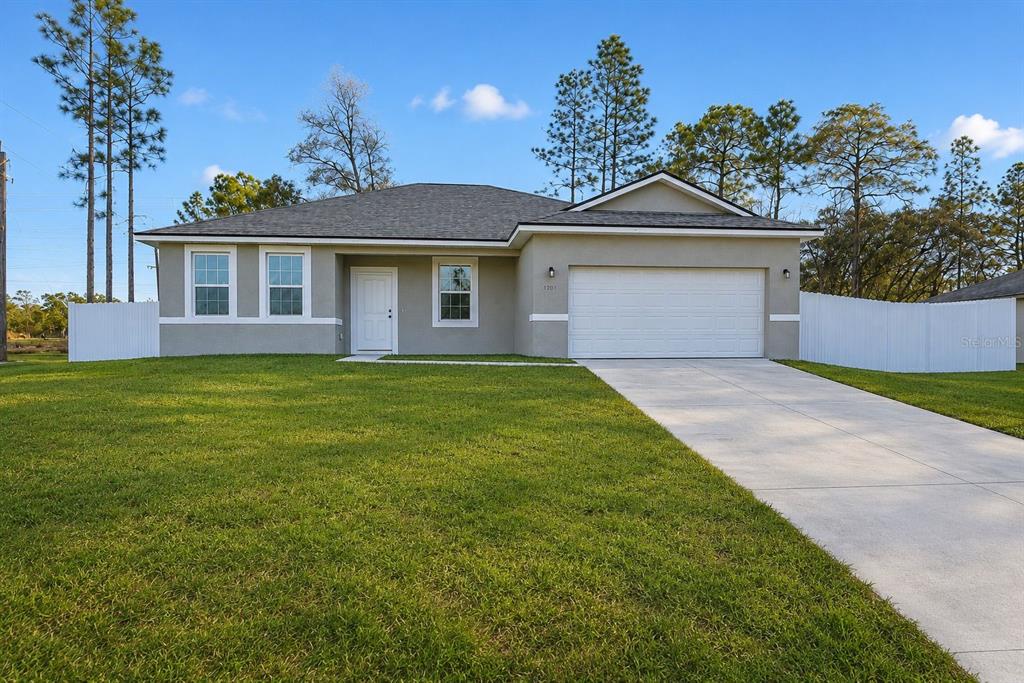 A single-story house with a gray stucco exterior, a two-car garage, and a white fence — 2701 W TRACY COURT, DUNNELLON, FL