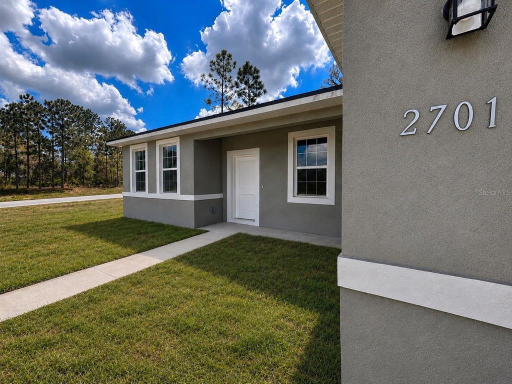 The exterior of a gray single-story house features a white front door and walkway — 2701 W TRACY COURT, DUNNELLON, FL