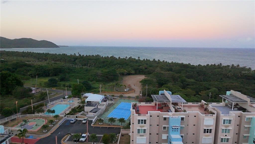 An aerial view shows a coastal apartment complex with a pool, tennis court, and ocean — Cond. VILLAS DEL FARO UNIT 3-301, MAUNABO, PR