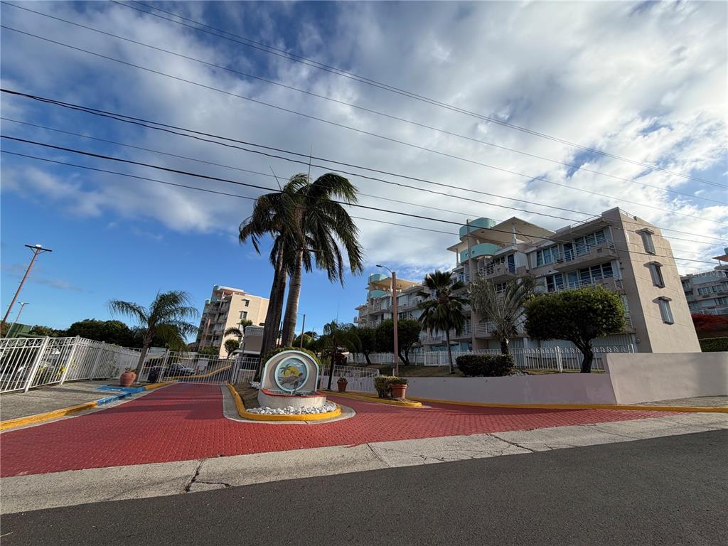 A paved driveway leads to the entrance of a multi-story apartment building with palm trees — Cond. VILLAS DEL FARO UNIT 3-301, MAUNABO, PR