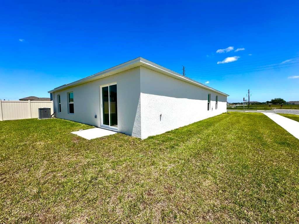 The exterior of a white stucco house features a sliding glass door and a small patio — 2102 CHRIS DRIVE, WINTER HAVEN, FL
