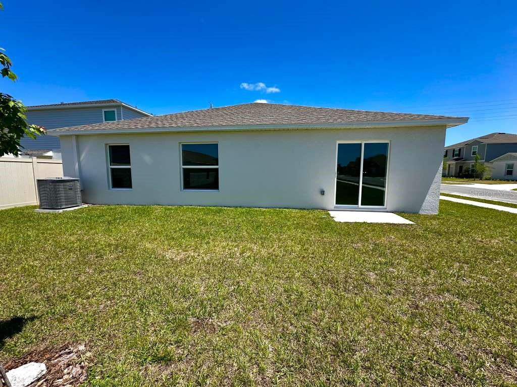 The exterior of a single-story house features a light-colored stucco wall, windows, and sliding doors — 2102 CHRIS DRIVE, WINTER HAVEN, FL