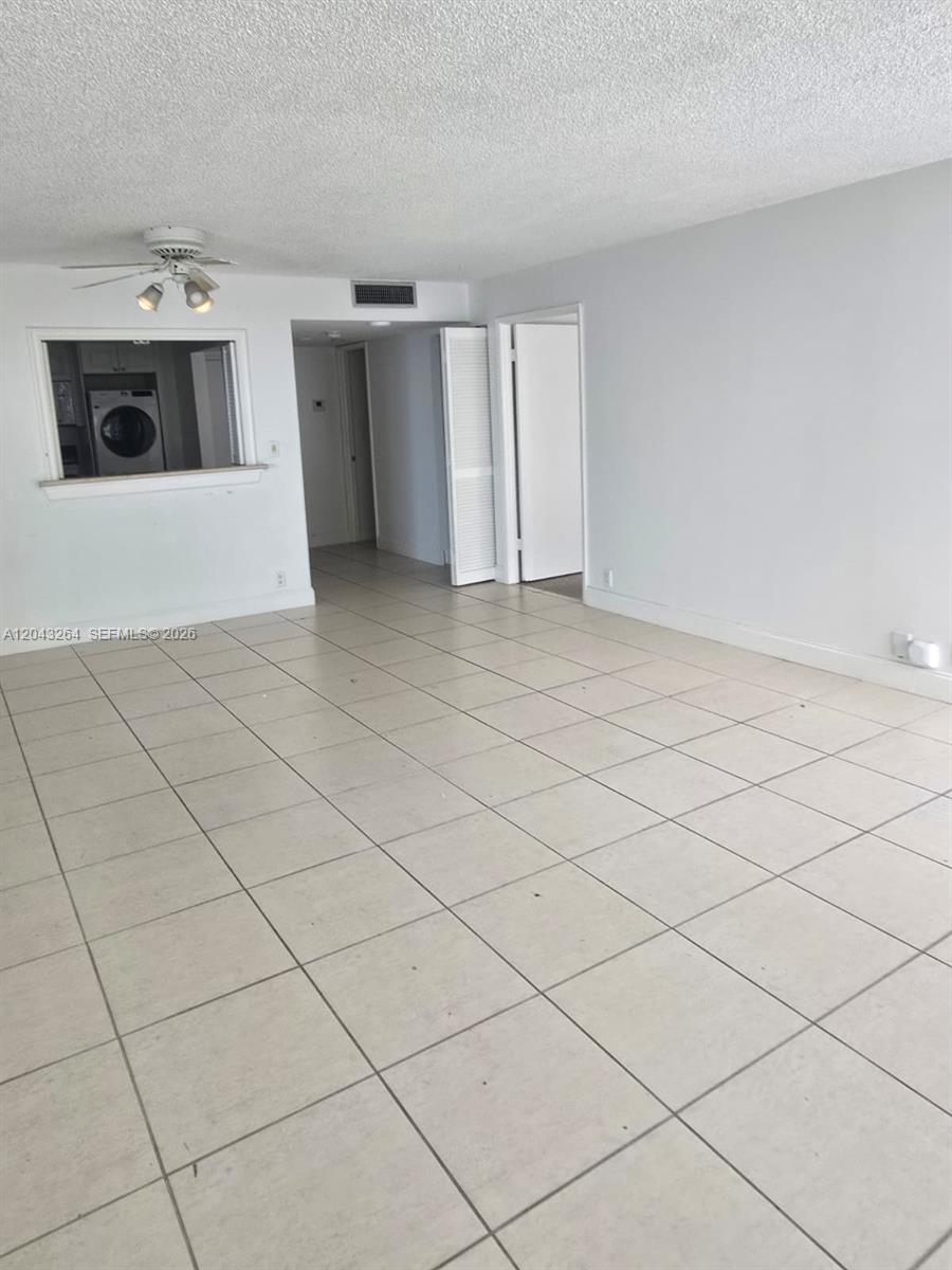 An empty room features white walls, light-colored floor tiles, a ceiling fan, and a pass-through window — 1901 Brickell Ave # B1007, Miami FL 33129, MIAMI, FL