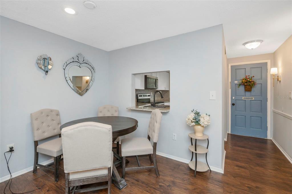 A dining area features a round wooden table, upholstered chairs, and a kitchen pass-through window — 4252 SHELDON PLACE UNIT 4252, NEW PORT RICHEY, FL