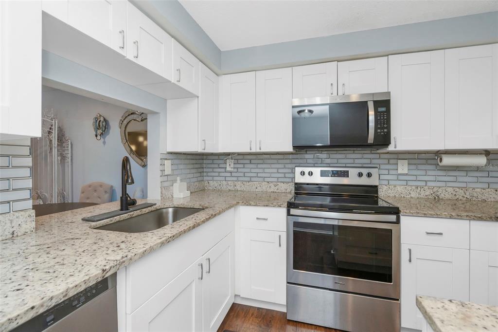 A kitchen with white cabinets, granite countertops, stainless steel appliances, and a gray subway tile backsplash — 4252 SHELDON PLACE UNIT 4252, NEW PORT RICHEY, FL