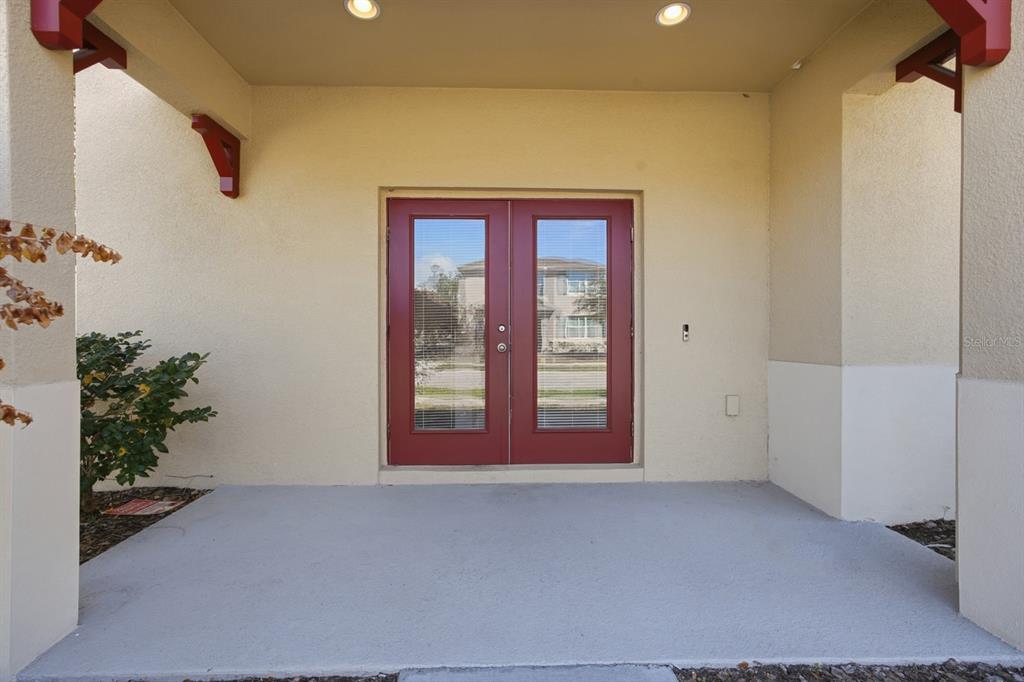 A covered concrete porch features red double doors with glass panels and recessed lighting — 1680 COULTER LANE, PORT ORANGE, FL